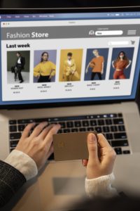 persona sosteniendo tarjeta de crédito en frente de un portátil mientras ve una pagina de ropa